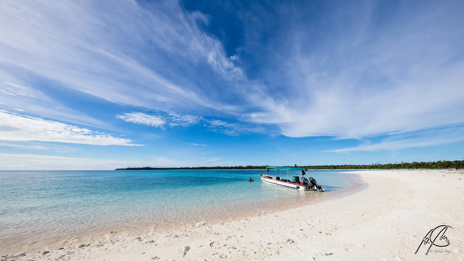 A white sand beach and moored boat under a wide blue sky