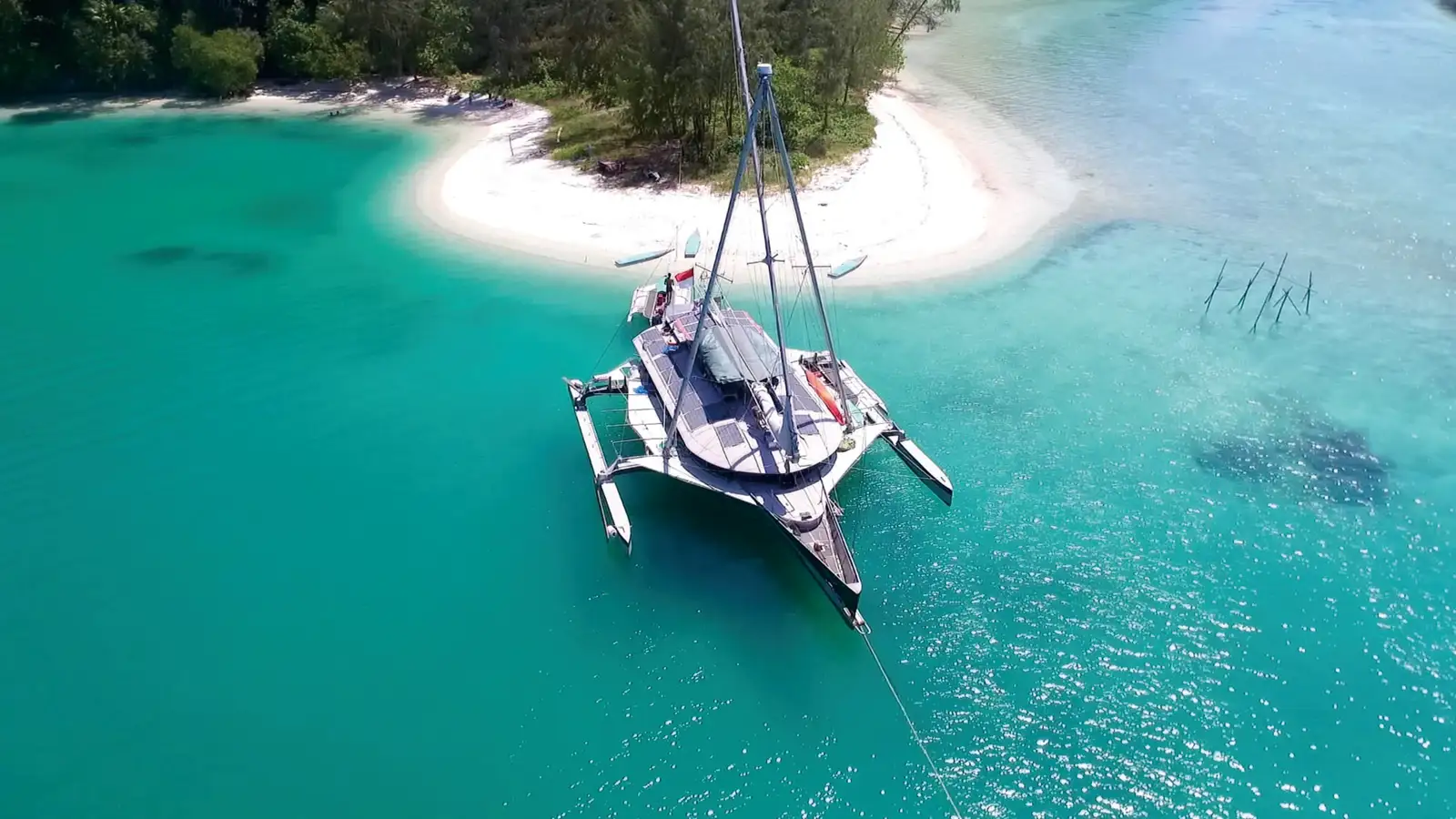 A sailing catamaran anchored off a white sand beach in clear shallow water