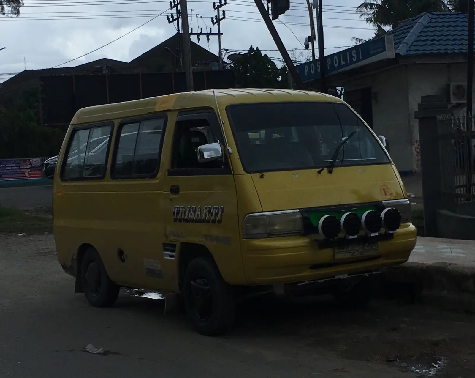 A yellow angkot minibus parked beside a police post in Sorong