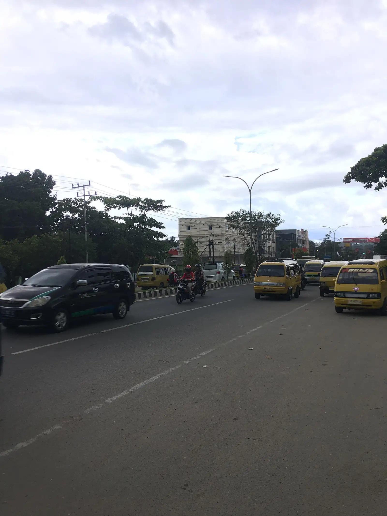 Yellow angkot minibuses and traffic on a main road through Sorong