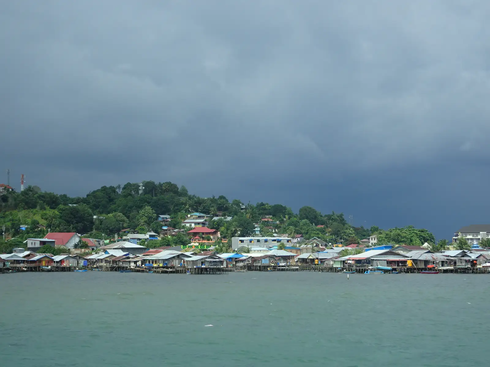 Stilt houses along the Sorong waterfront under a dark storm sky