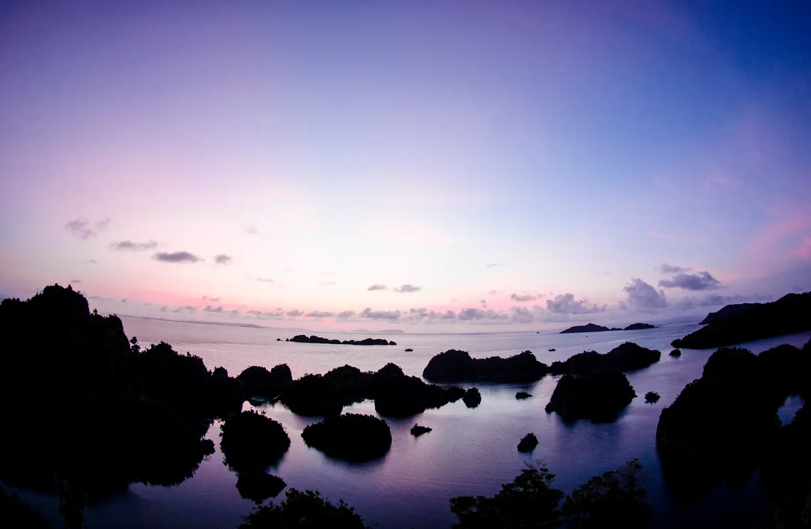 Pink and violet dawn sky over rocks and calm water at Pianemo