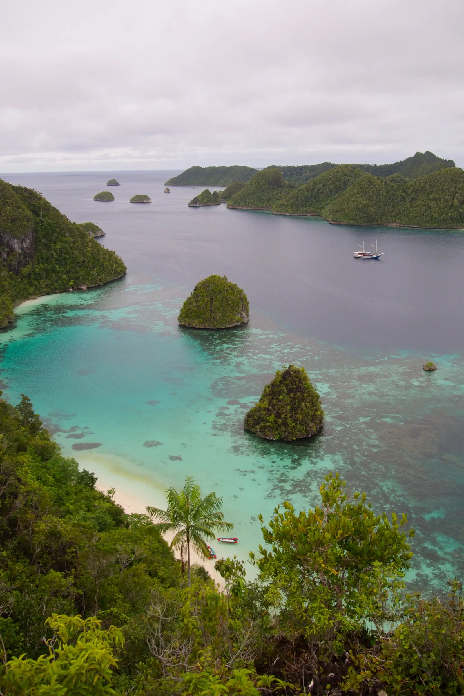 A yacht anchored among Wayag's karst islets above a turquoise reef flat